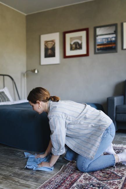 A person is vacuuming a patterned, traditional-style carpet with a black upright vacuum cleaner. The vacuum head is positioned flat on the carpet's floral design, which features soft pastel colors and